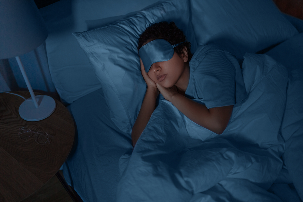 woman sleeping in dark bedroom with eye mask