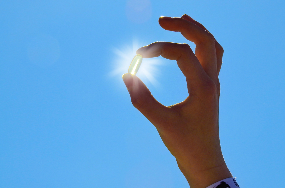 vitamin D pill held up in front of sun in blue sky