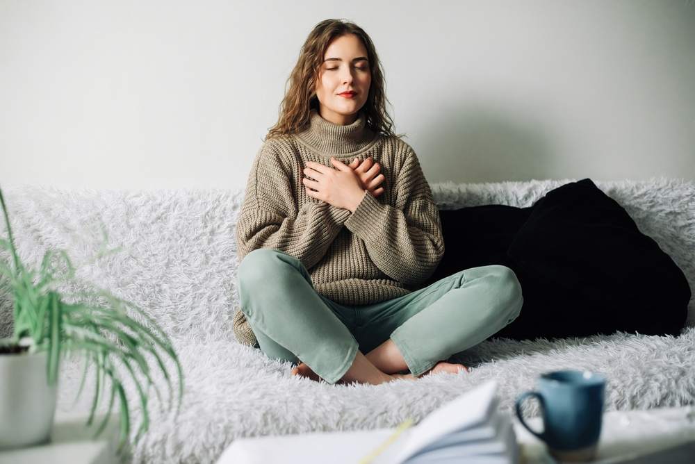 woman practicing deep breathing exercises while sitting on couch