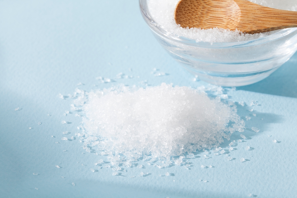 wooden spoon scooping Epsom salt from glass bowl to tabletop