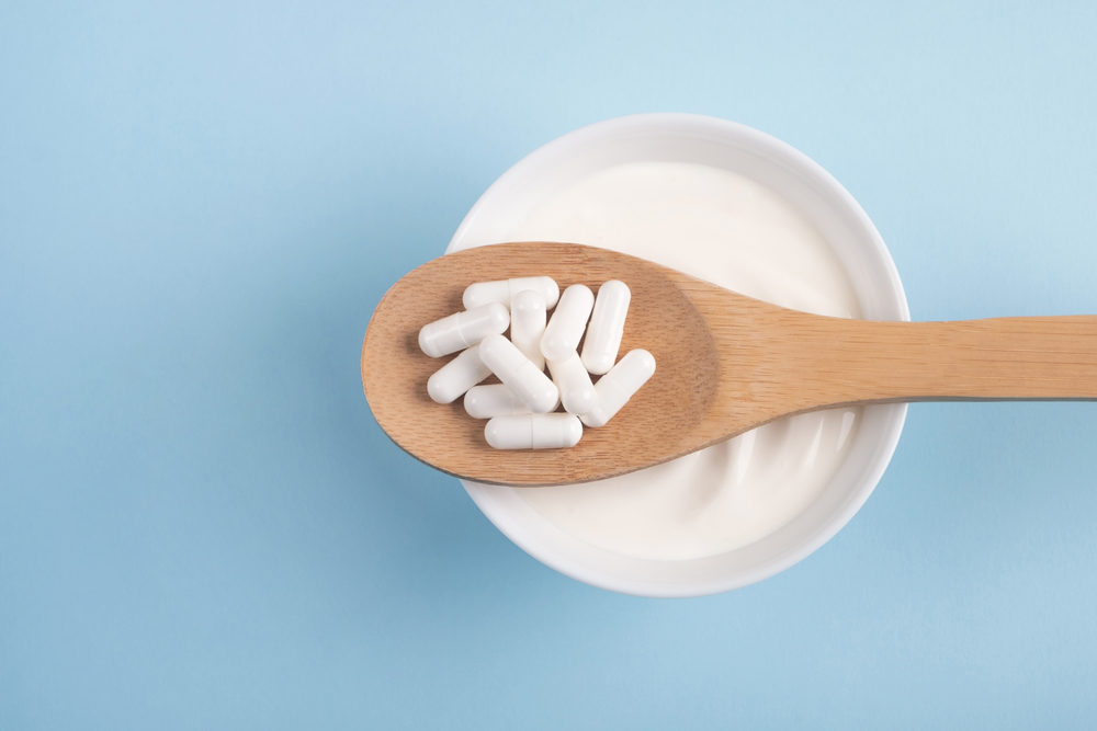 wooden spoon filled with probiotic supplements over bowl of yogurt