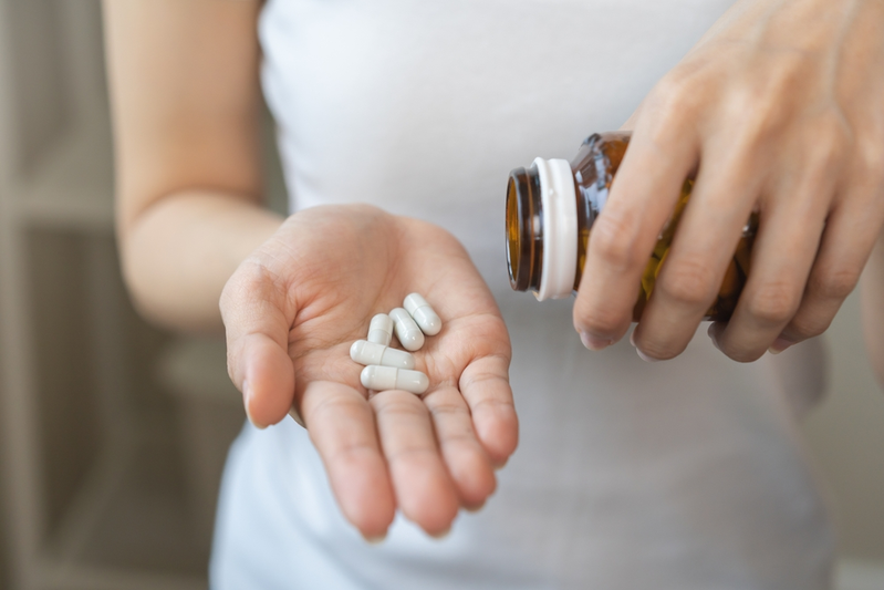 close up of woman pouring dietary supplements from bottle into hand